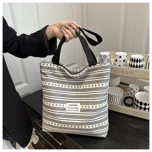 Détail du sac cabas en toile rayée noir et blanc avec poignées tissées et écusson