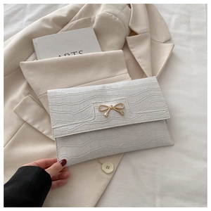 Detail of white stone-patterned envelope bag with golden bow and crocodile texture