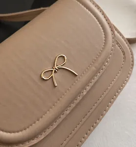 Detailed view of a stylish khaki saddle bag featuring a chic gold bow-knot buckle
