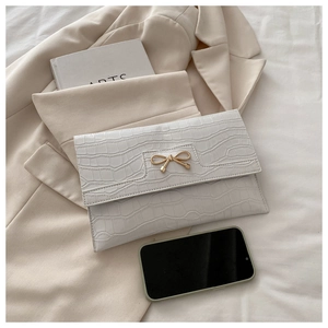 Detail of white stone-patterned PU handbag with golden bow accent and elegant texture