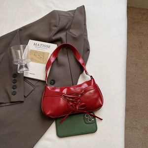 Chic red patent leather underarm bag with bow tie detail on a grey blazer
