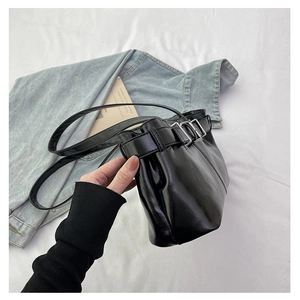 Close-up of black glossy shoulder bag featuring three parallel silver metal buckles