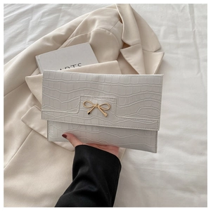Close-up of white crocodile pattern PU leather clutch with golden bow metal buckle