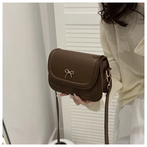Gros plan d'un sac besace marron avec une décoration délicate en forme de nœud en métal