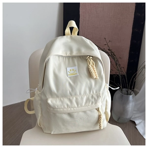 Close-up of cream backpack featuring yellow smiley face patch and woven rope zippers