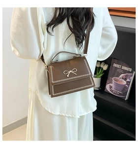 Detalle de bolso bandolera marrón con lazo dorado y costuras blancas sobre el modelo
