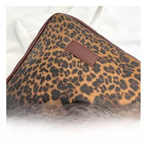 Detailed close-up of leopard print tote bag material with brown leather trim and texture