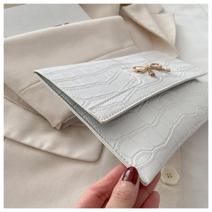 Detail of white crocodile texture clutch bag featuring a gold bow metallic clasp