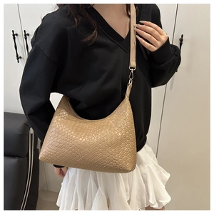 Detail of a beige PU leather underarm bag with woven texture worn by a model in black outfit