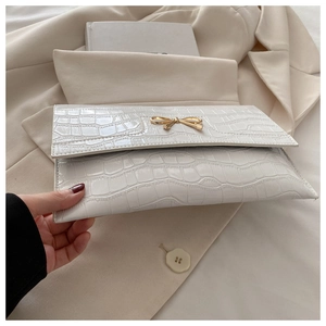 Detail of white crocodile pattern clutch bag featuring a gold bow buckle on beige suit