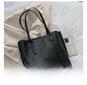 Top view of a black faux leather tote bag with long straps next to a smartphone