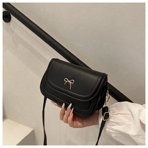Sac à bandoulière noir minimaliste avec détail nœud doré tenu à la main