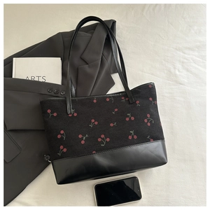 Detail of black corduroy tote bag with red cherry print and leather base on lifestyle background