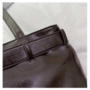 Macro shot of dark brown oil wax leather texture and stitching detail on underarm bag