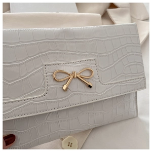 Detailed view of white crocodile pattern PU leather handbag with golden bow metal buckle