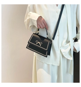 Elegante bolso bandolera negro con un lazo dorado y detalles únicos de bordes cosidos