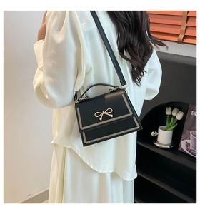 Primer plano de un elegante bolso bandolera negro con lazo dorado y pespuntes