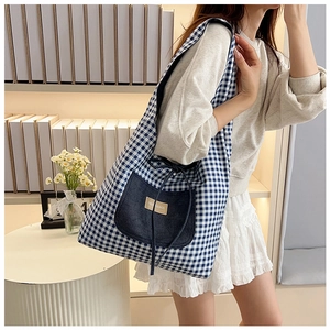 Close-up of blue plaid canvas tote bag featuring a denim pocket with a leather brand label