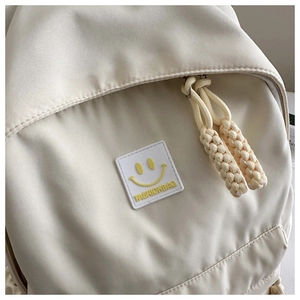 Gros plan d'un sac à dos en toile crème avec un patch smiley et une tirette de zip tissée