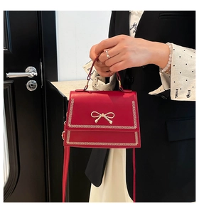 Primer plano de un bolso de cuero rojo con lazo dorado y correa de hombro