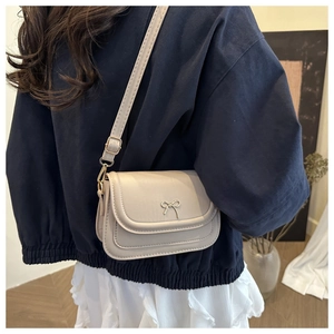 Détail d'un petit sac à bandoulière beige minimaliste avec un nœud en métal doré