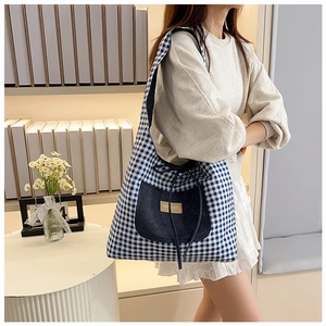 Detail of blue gingham tote bag featuring a denim pocket and leather fashion label