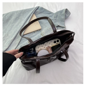 Macro shot showing the spacious interior of a dark brown glossy leather tote bag with items