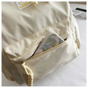 Détail de la poche avant et logo sur sac à dos en nylon crème avec rangement téléphone
