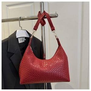 Close-up detail of a textured red woven shoulder bag hanging on a silver metal clothing rack