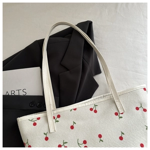 Detail of white tote bag with red cherry print and slender shoulder straps