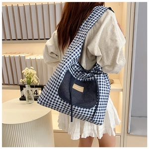Detailed shot of a blue gingham shoulder bag with denim pocket and leather tag