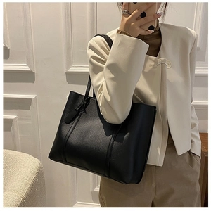 Model wearing a large black matte leather tote bag with side strap details for daily use