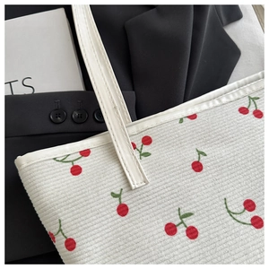 Detail of white corduroy tote bag featuring red cherry prints and white leather straps