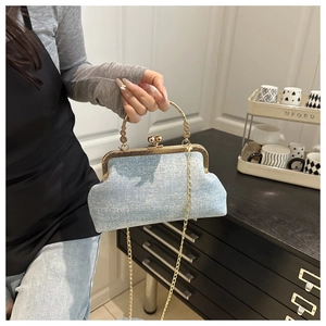 Detail of a light blue denim-textured shell bag with gold handle and chain strap.