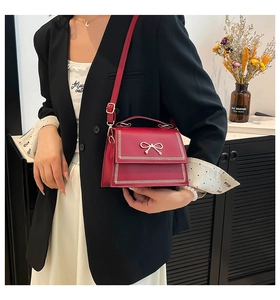 Elegante bolso bandolera rojo con lazo de metal, lucido por una modelo con una chaqueta.