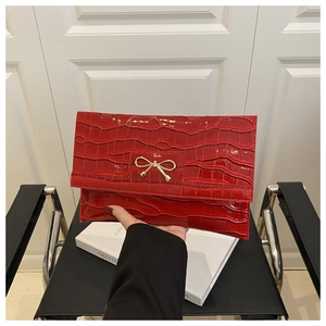 Macro detail of red faux crocodile leather clutch featuring a golden bow metal buckle