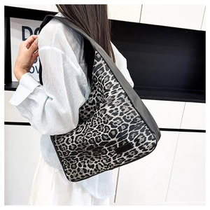Detail view of large leopard print tote bag with black leather straps on woman's shoulder