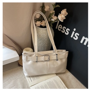 Detail view of cream shoulder bag with silver buckle and thin straps on a beige background
