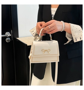 Detalle de bolso bandolera blanco elegante con lazo dorado sostenido por una modelo