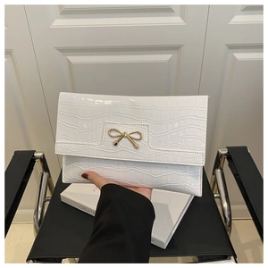Detail of white crocodile texture envelope clutch with a gold bow metal clasp