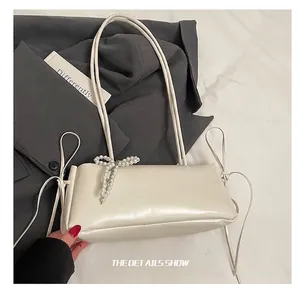 Detail showing white leather underarm bag with elegant pearl bow and thin shoulder straps