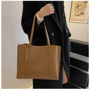Brown leather tote bag worn over the shoulder with a black coat for commute style