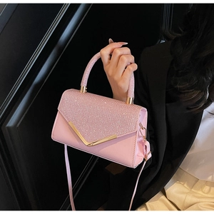 Detail van een roze crossbodytas met strass-flap en gouden V-vormige versiering
