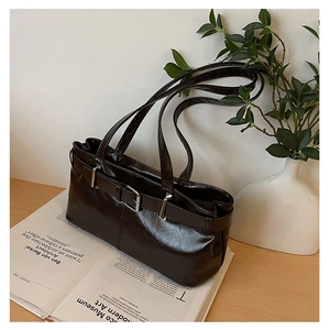 Detail of retro dark brown glossy underarm bag with silver buckle on a magazine