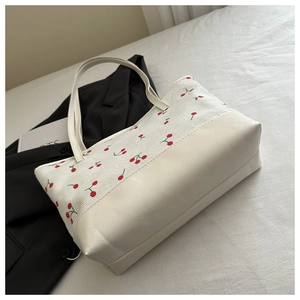 Detail of canvas tote bag with cherry print and faux leather base on a soft bed