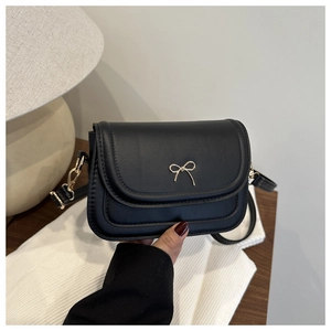 Élégant sac besace noir avec un détail de nœud doré présenté dans un cadre de vie quotidien.
