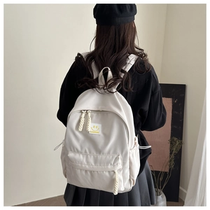 Detail of a white minimalist nylon backpack featuring a smiley patch and woven rope zipper pulls