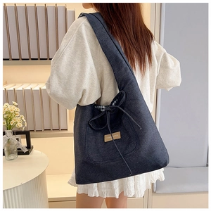 Detail of denim tote bag with brown leather logo and decorative bow on shoulder strap