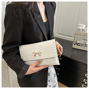 Close-up of a white faux leather envelope clutch with stone pattern and gold bow detail