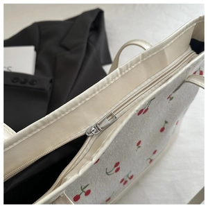Detailed close-up of smooth silver zipper and red cherry print on white tote bag